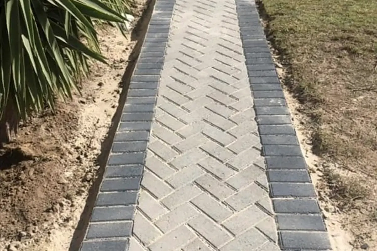 Finished herringbone paving pathway edged in charcoal brick through a garden