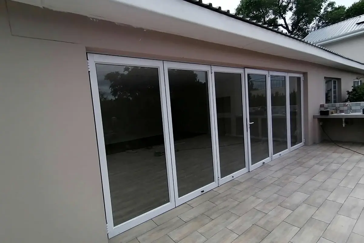 Tiled patio with new folding glass doors along the back of a house