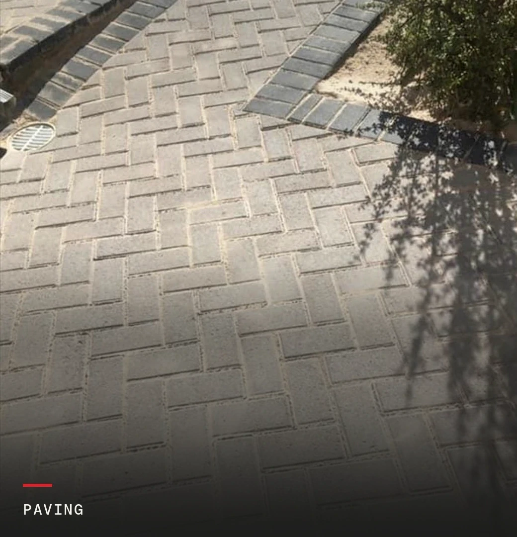 Newly laid herringbone paving with a charcoal border running past a stormwater drain, labelled: paving.